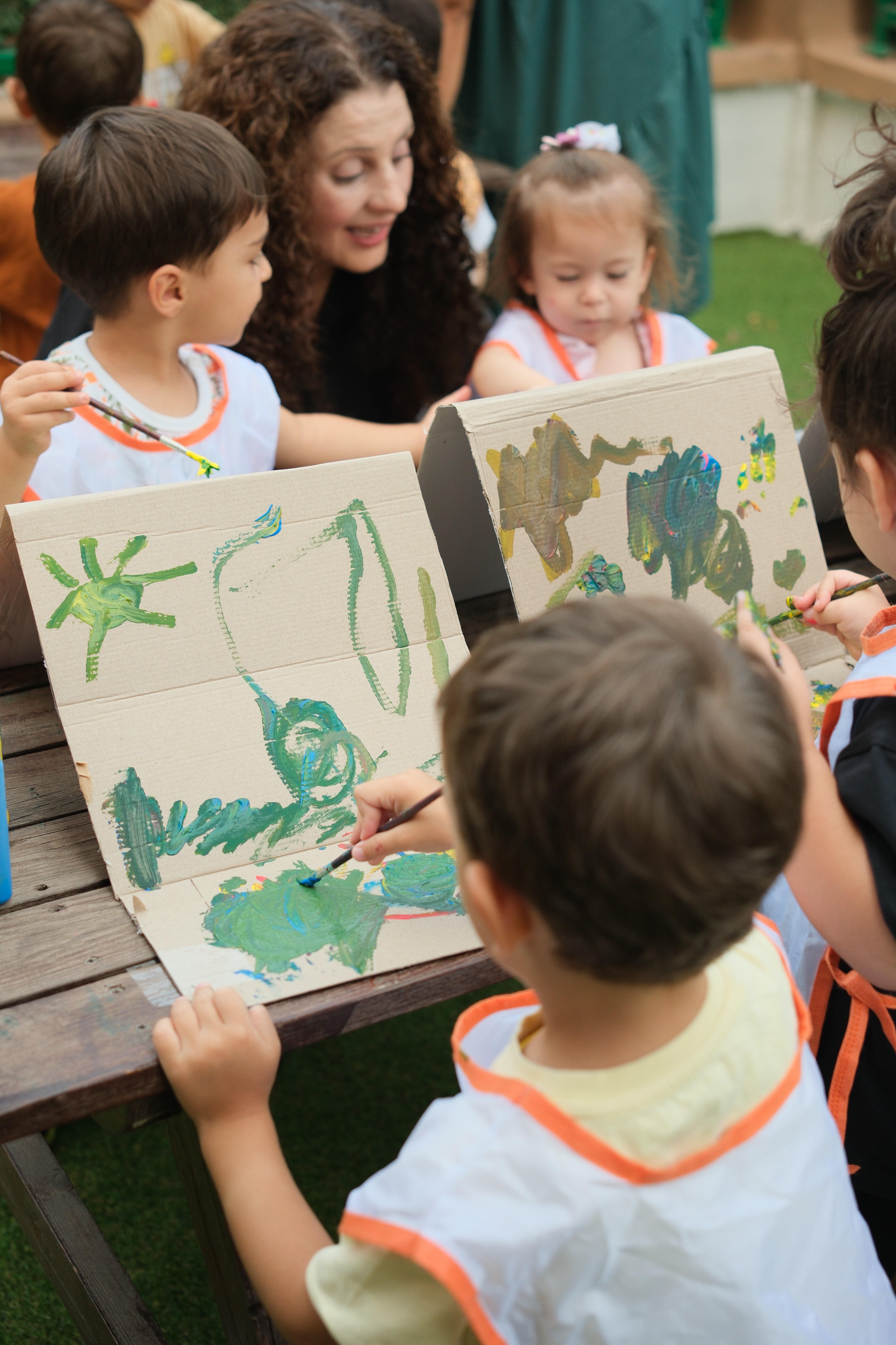 Açık alanda sanat çalışmasını paylaşan okul öncesi çocuklar